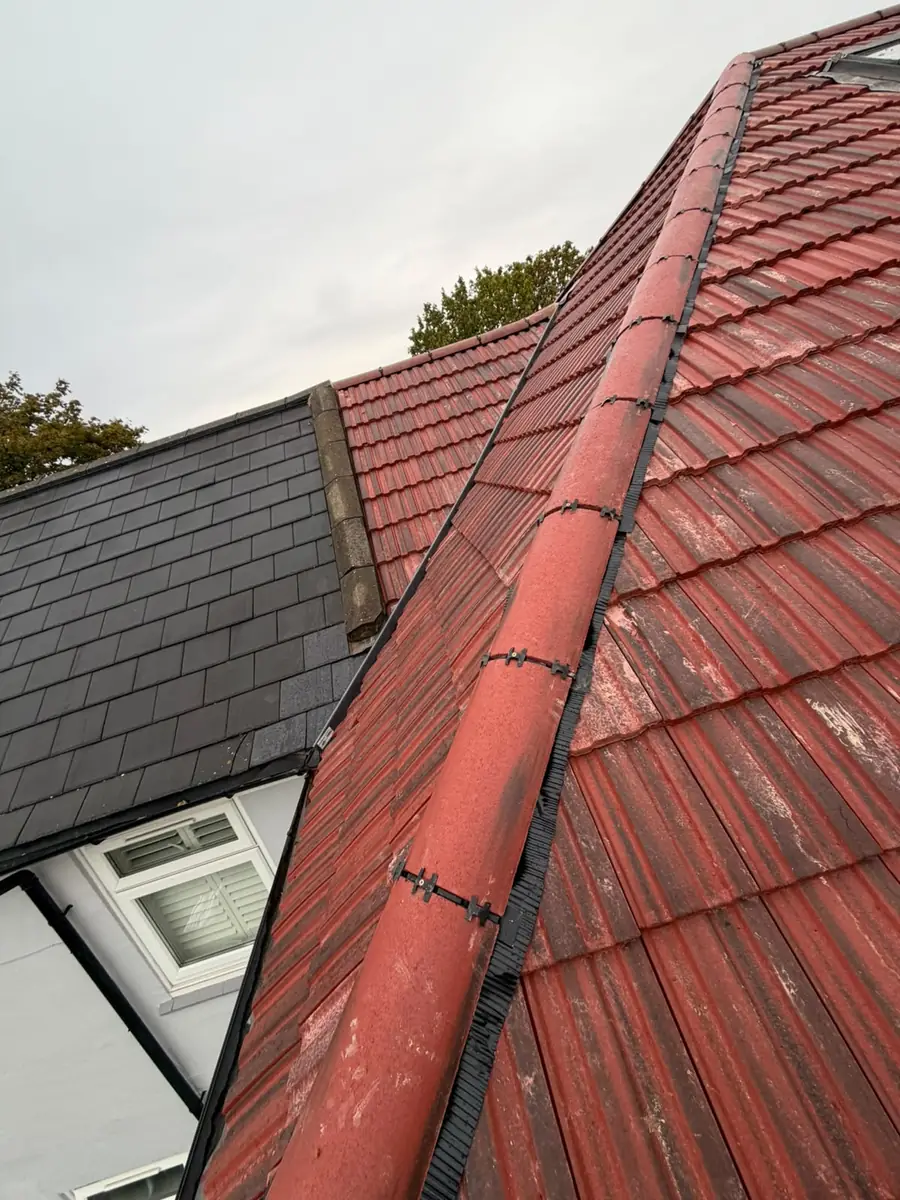 Ventilated dry ridge on red interlocking tiles next to the neighbour's slate roof in East Ham