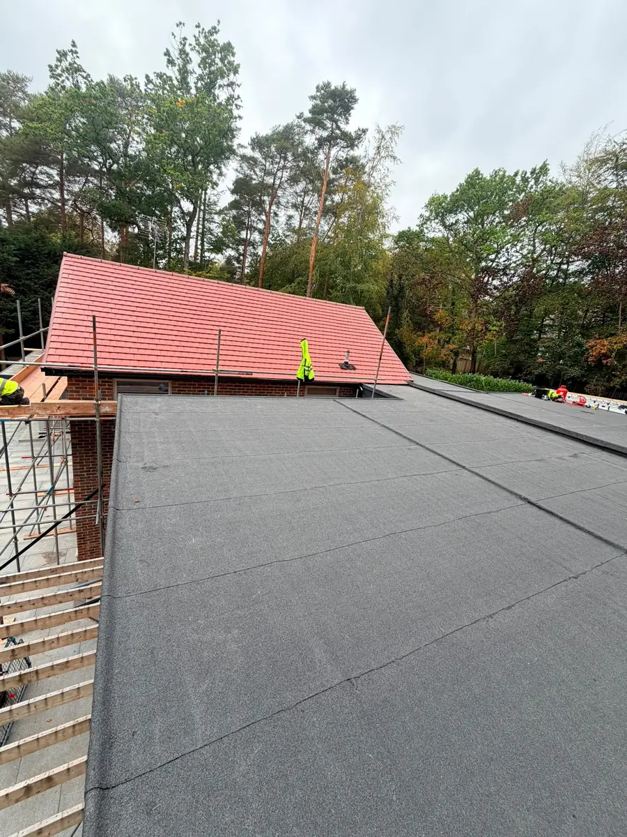 Large new felt flat roof with grey mineral cap sheet and the new tiled roof beyond in Fleet