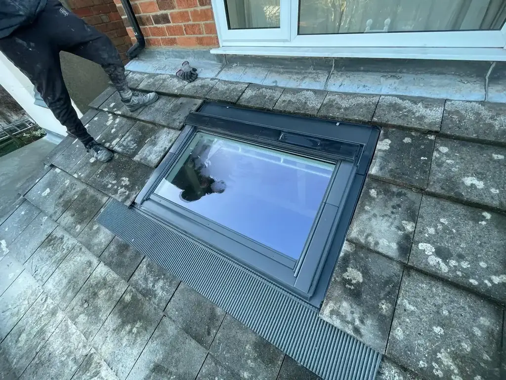 Roof window with its grey flashing kit fitted into a tiled lean-to roof