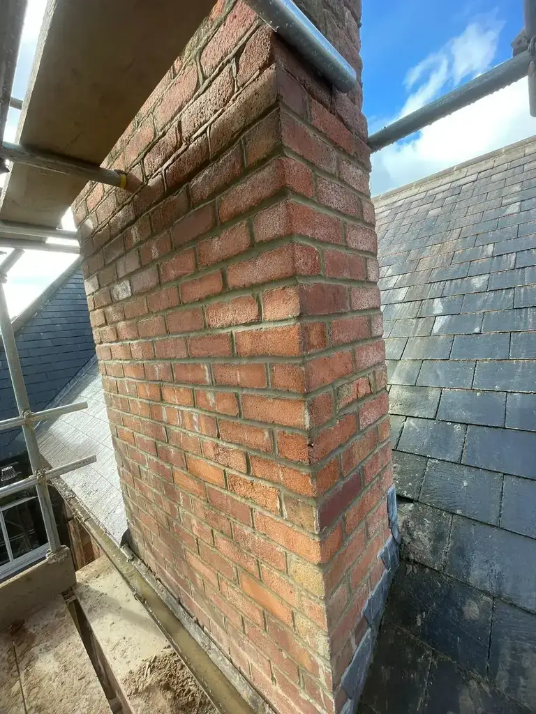 Brick chimney stack with weathered mortar joints rising through a slate roof